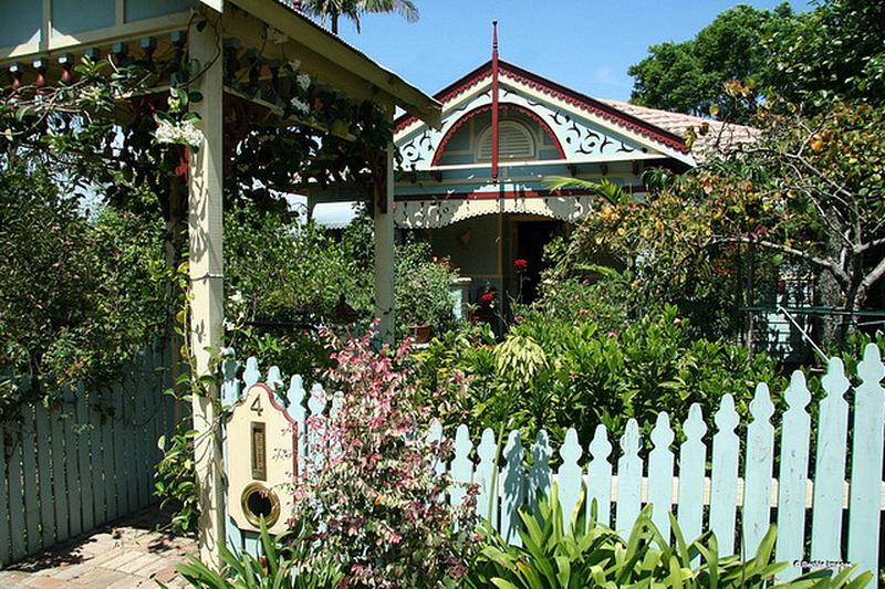 A cottage with iron lace verandah behind a picket fence and cottage garden in Asquith