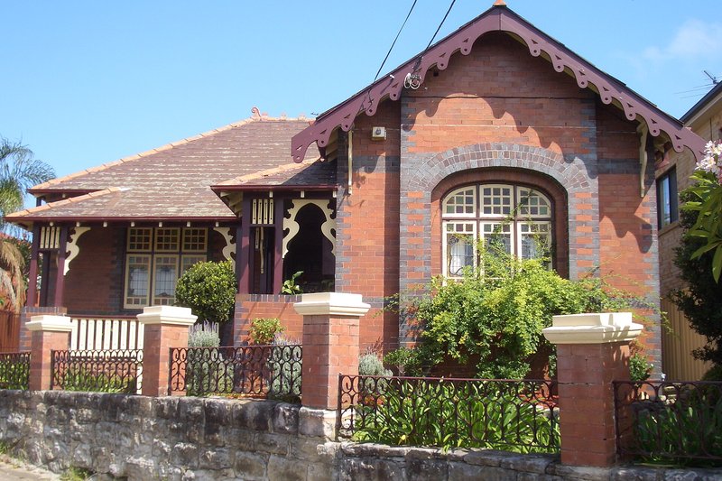 A Federation brick bungalow with leadlight windows behind a sandstone and iron fence, Bardwell Valley