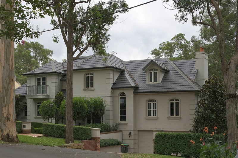 A large rendered two-storey house behind clipped hedges and gum trees at Beecroft
