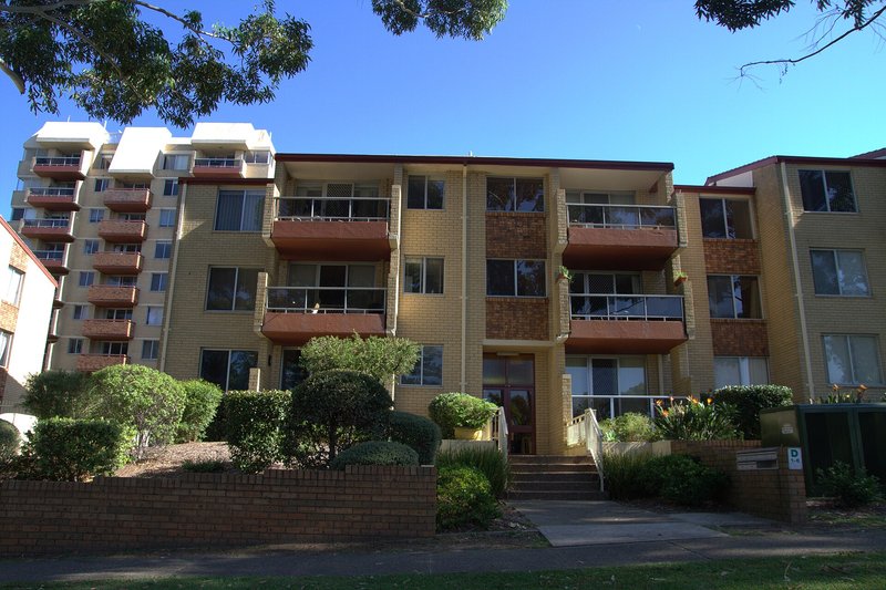 Yellow brick walk-up apartment blocks behind clipped hedges in Caringbah