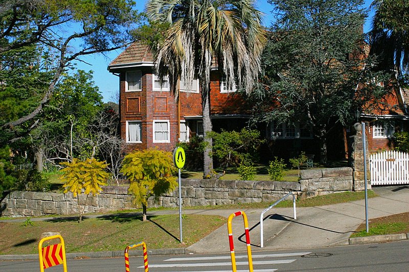 A two-storey brick house behind a sandstone wall opposite Cheltenham station