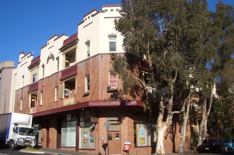 Corner block of flats and a gallery in Chippendale, with paperbarks along the footpath