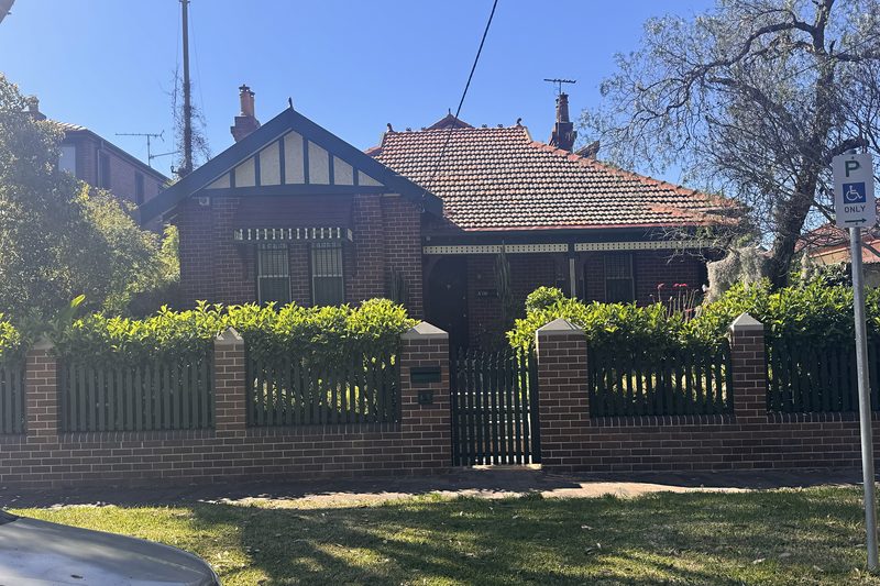 A Federation brick bungalow behind a clipped hedge and picket fence in Kensington