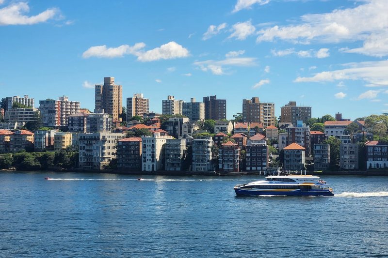 Apartment blocks stacked along the Kirribilli waterfront, with a ferry crossing the harbour
