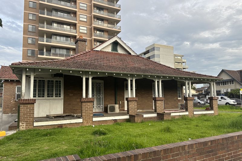 The former Lidcombe police station, a low brick building with apartment towers rising behind it