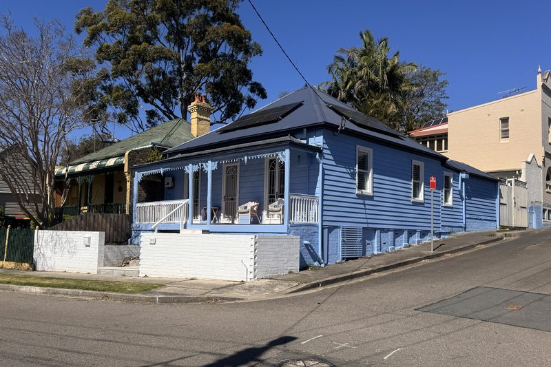 A blue weatherboard Victorian cottage with verandah lace on a Lilyfield corner