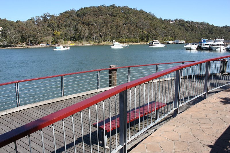 The riverside boardwalk at Lugarno looking across the Georges River to moored boats and bushland
