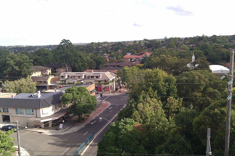 Elevated view over a shopping strip corner and the tree-covered streets beyond in Miranda
