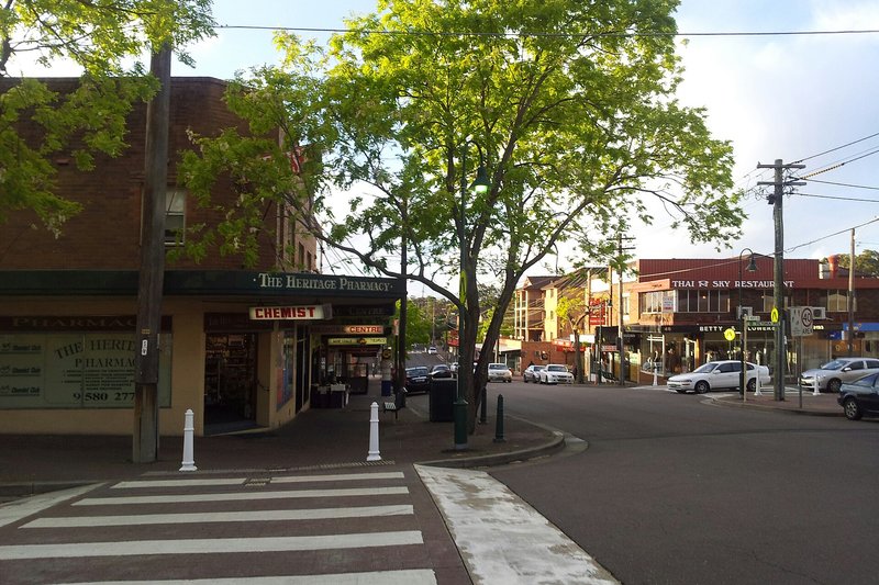 The shopping strip and pharmacy corner at Mortdale, with jacarandas along the footpath