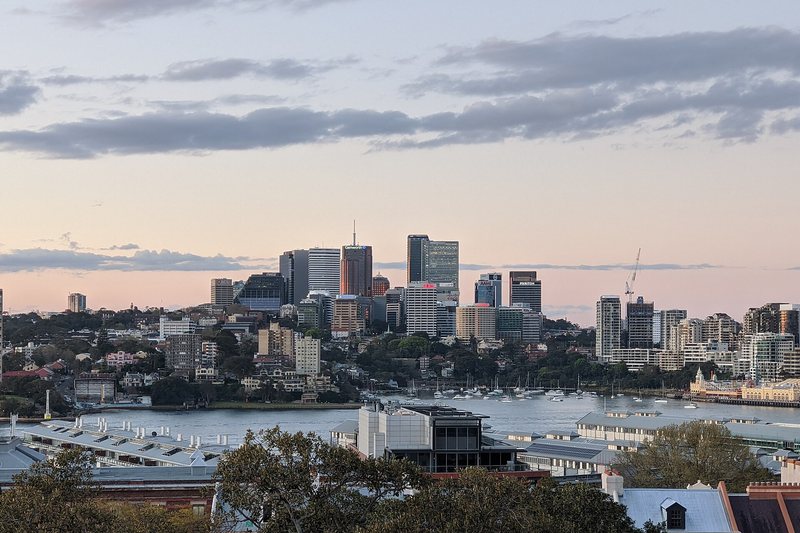 The North Sydney office towers at dusk, above the harbour and moored boats