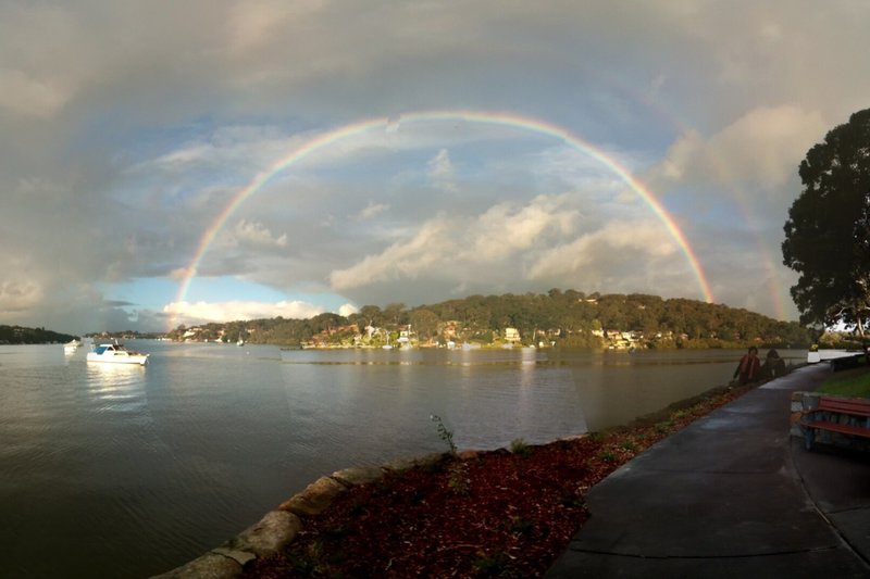 A rainbow arcing over the water and wooded shoreline at Oyster Bay