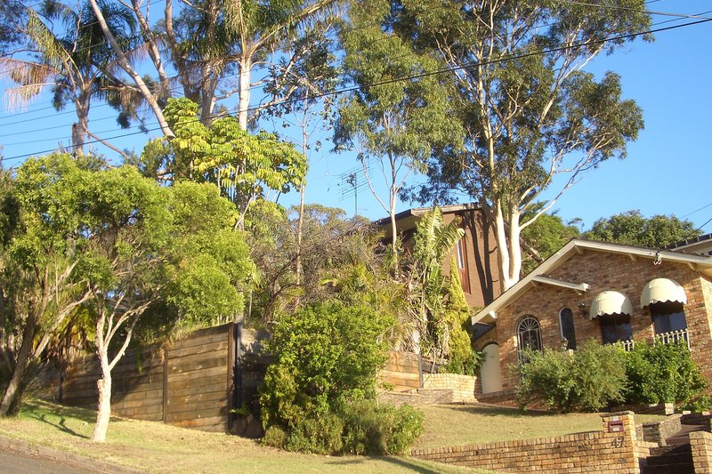 A brick home set among gums and palms on a sloping street at Padstow Heights