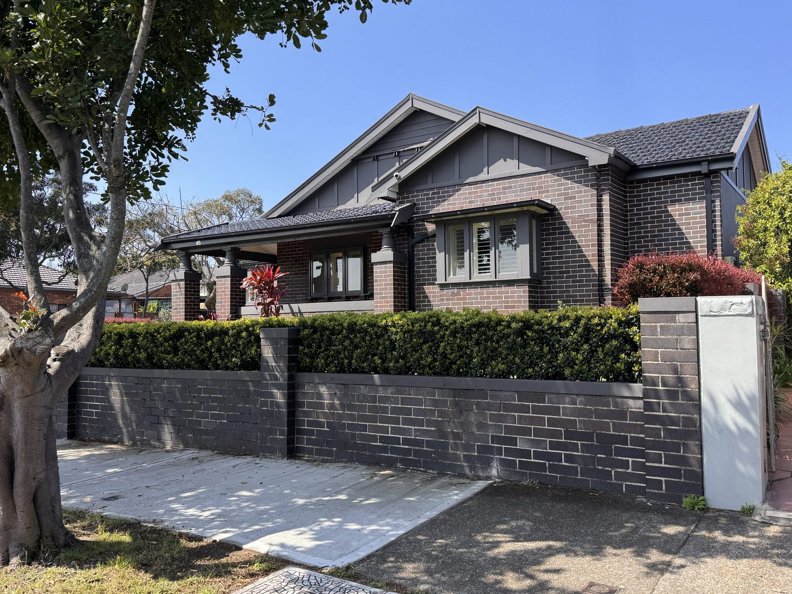 Brick bungalow with twin gables, a shaded verandah and a clipped hedge in Rosebery.