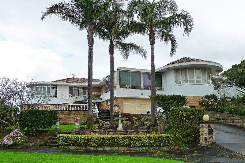 A curved mid-century house behind cocos palms on a Roseville Chase street