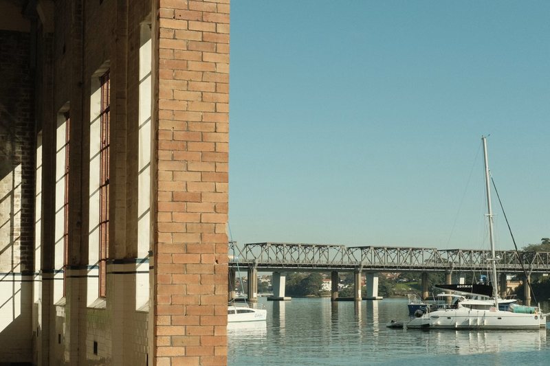 Brickwork of an old industrial building at Rozelle, with boats and the rail bridge on the bay beyond