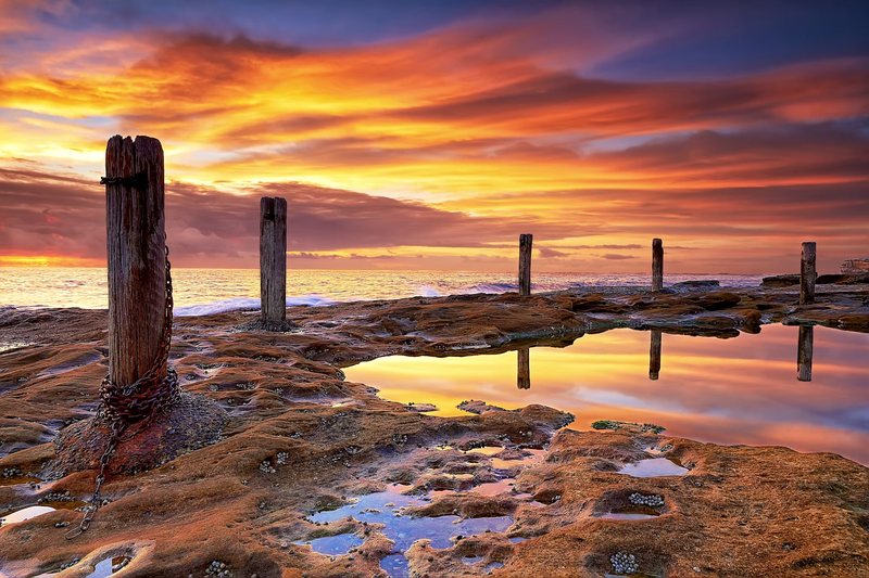 Sunrise over the Ivo Rowe rock pool and its timber posts at South Coogee
